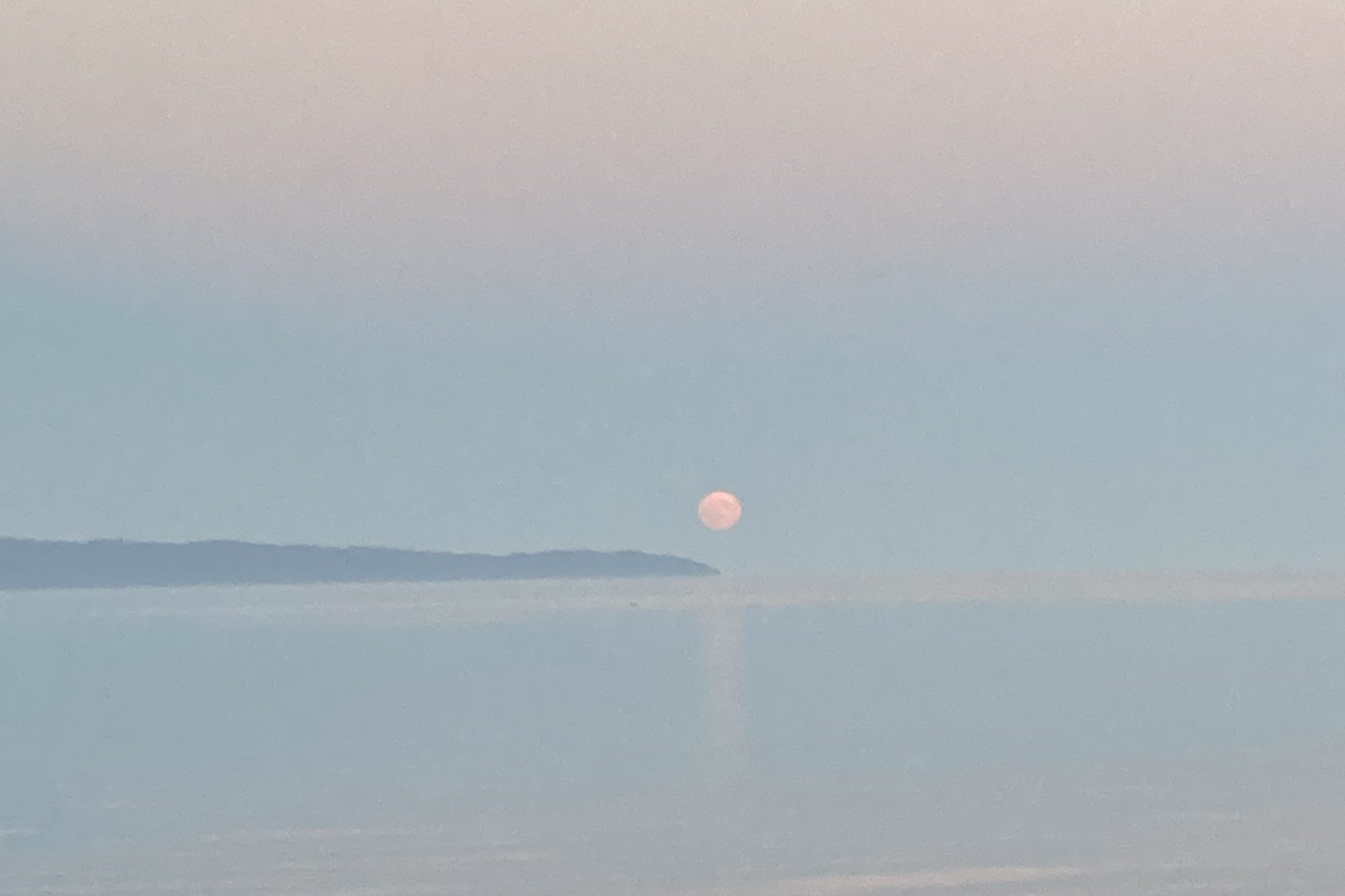 A photograph taken in autumn 2024 in Gaspé, Quebec in Canada of a super moon rising off the end of a peninsula at dusk. 